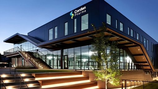 The CordenPharma building at dusk with dark cladding, large glass windows, and illuminated entrance steps