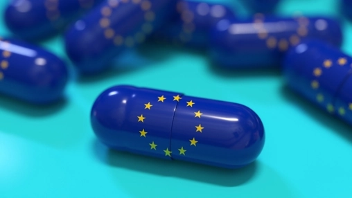 Close-up of a blue capsule bearing the EU flag circle of stars against a teal background with blurred capsules
